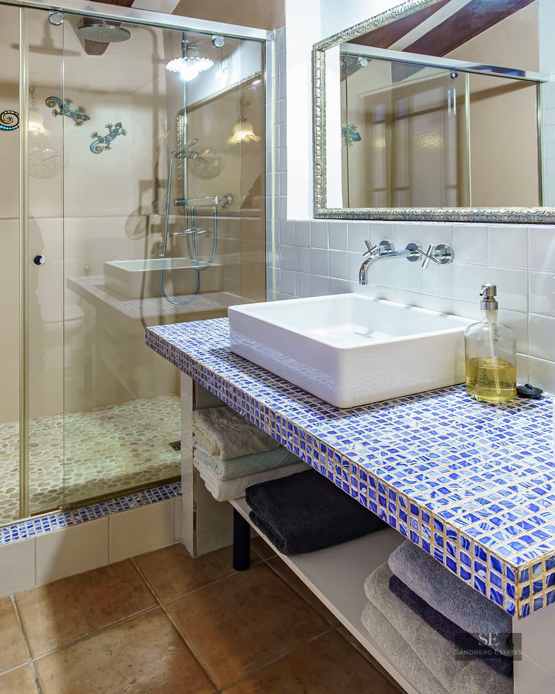 Modern bathroom featuring a walk-in shower with pebble floor and a blue mosaic tile vanity with a white vessel sink.