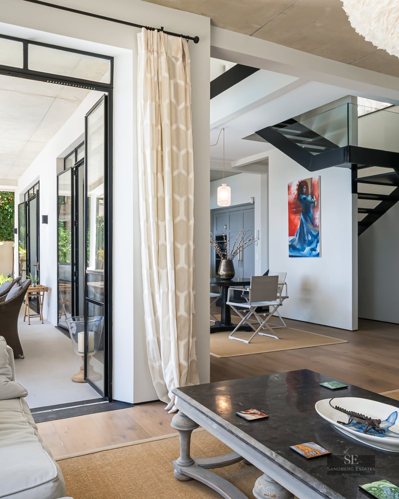 Modern living room with grey sofas, a large white feather lamp, and glass doors opening to a lush terrace.
