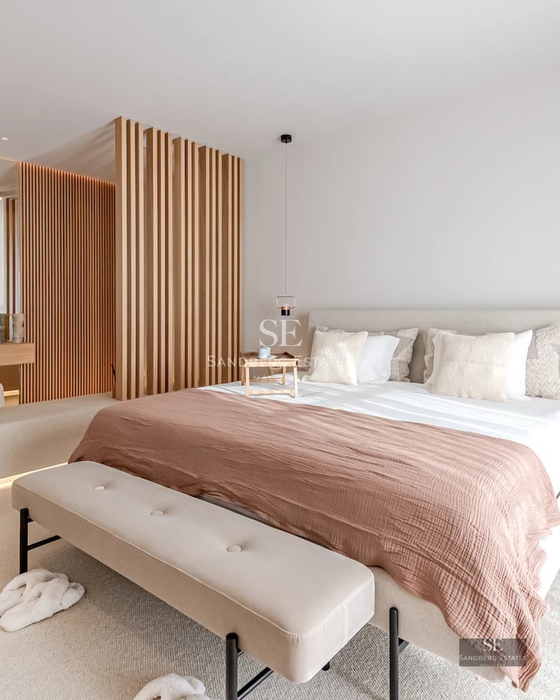 Exterior view of a modern luxury home with infinity pool, wooden deck, and large glass windows. Contemporary design and manicured landscaping.