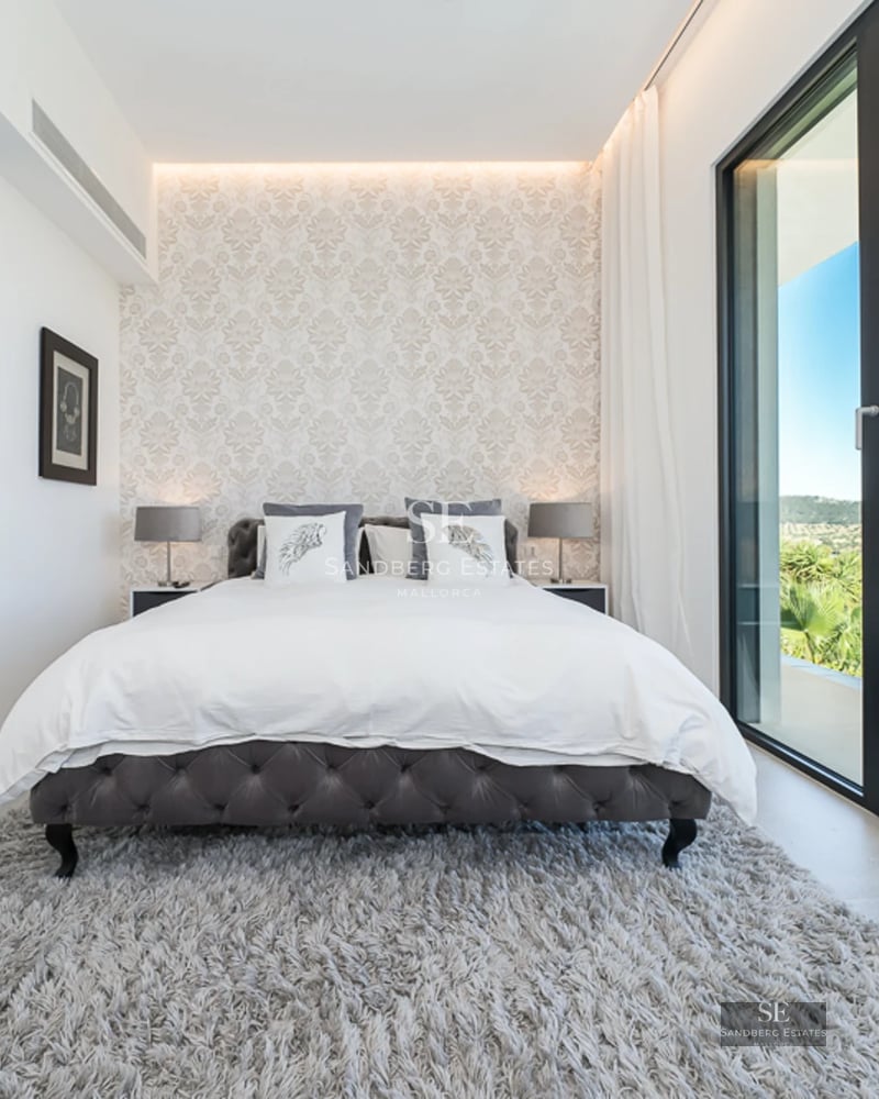 Spacious living room with large windows, light wood floors, natural lighting, and minimalist decor. View of a lush garden.