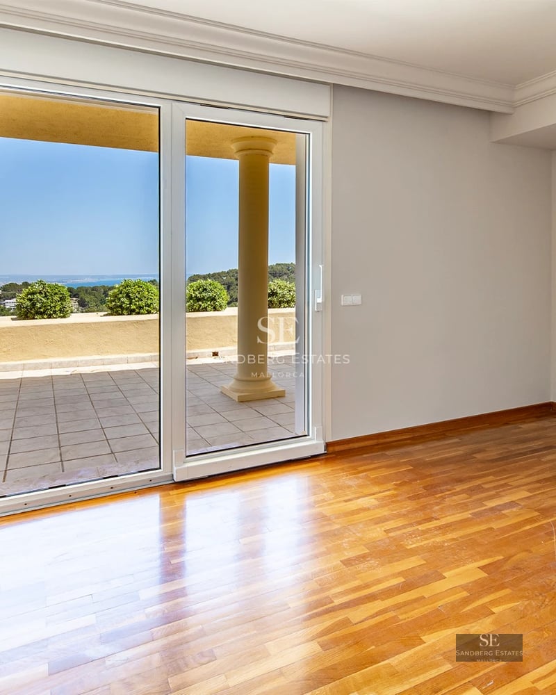Spacious living room with floor-to-ceiling windows, light wood floors, white walls, and modern design furniture. Abundance of natural light.