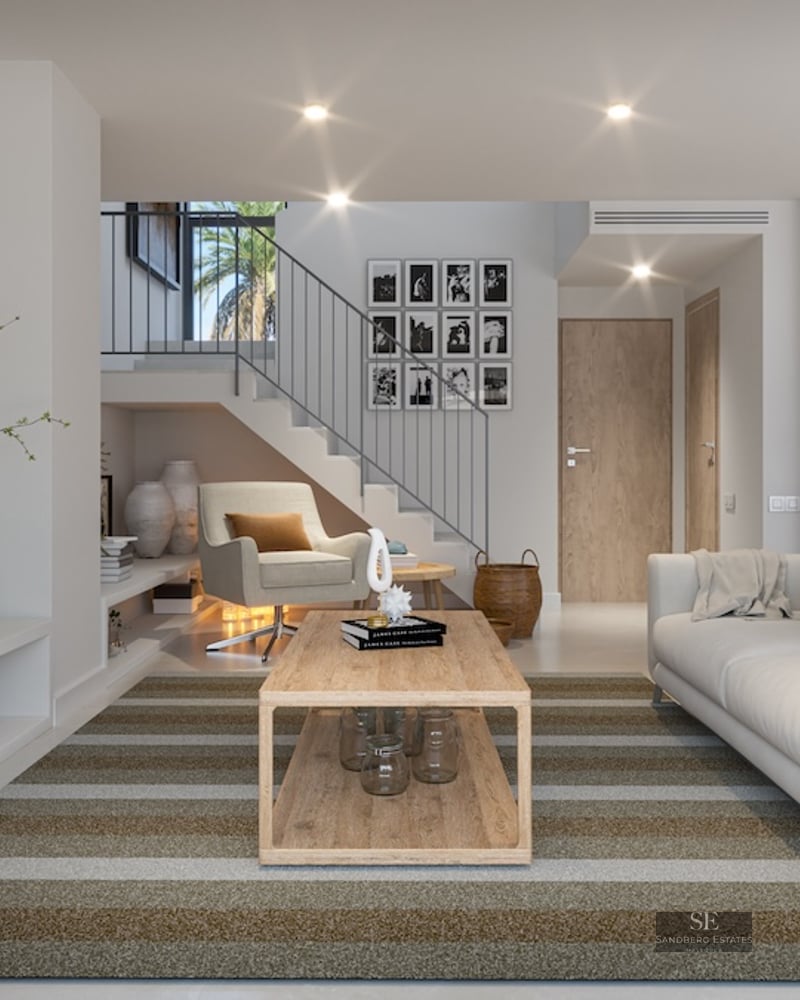 Bright living room featuring a white sofa, wooden coffee table, striped rug, and a modern staircase in the background.