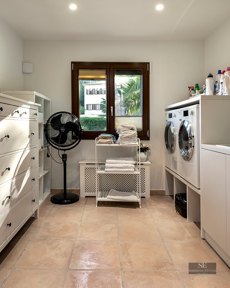 Clean laundry room with white cabinetry, washer, dryer, and terracotta tile flooring under natural light.