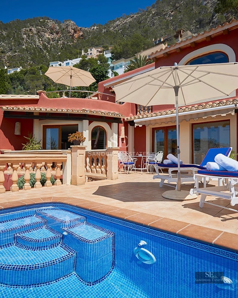 View of an elegant modern villa with reflecting pool, large windows and lush tropical garden.