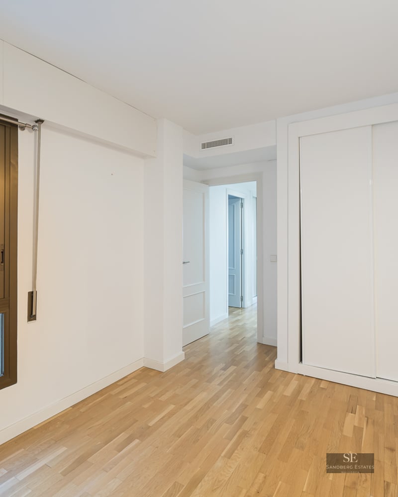 Empty room with light wood floors, a white built-in sliding door closet, and a large window with a bronze frame.