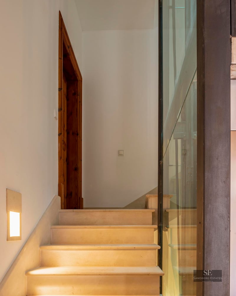 Stone steps leading up next to a glass wall and wooden door frame, illuminated by warm wall lights.