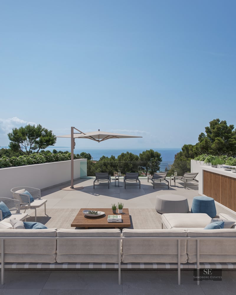 Large modern terrace with sofas, sunbeds, and an expansive view of the sea under a clear blue sky.