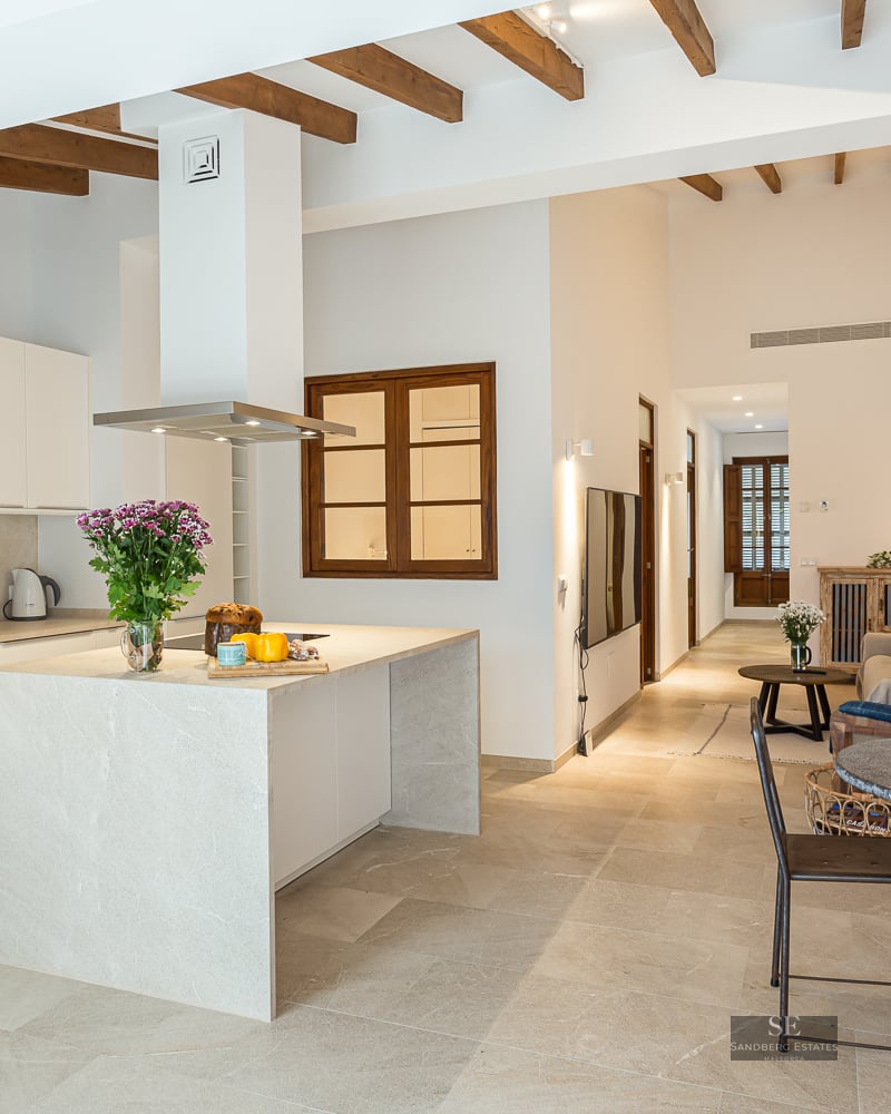 Bright open-plan kitchen featuring a stone island, wooden ceiling beams, and a rustic dining area.