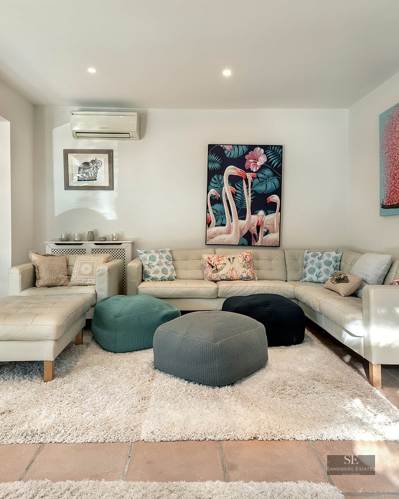 Modern living room featuring a white leather sectional sofa, colorful poufs, a plush rug, and a wood-burning fireplace.