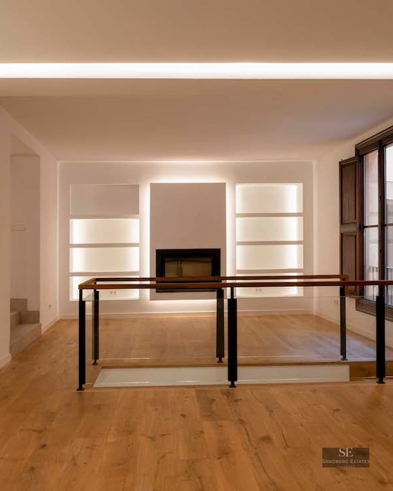 Minimalist interior with light oak floors, white walls featuring LED-lit niches, and a glass-railed staircase landing.