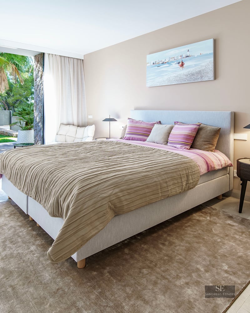 Chambre moderne avec grand lit, lampes design et baies vitrées ouvrant sur une terrasse de jardin luxuriante.