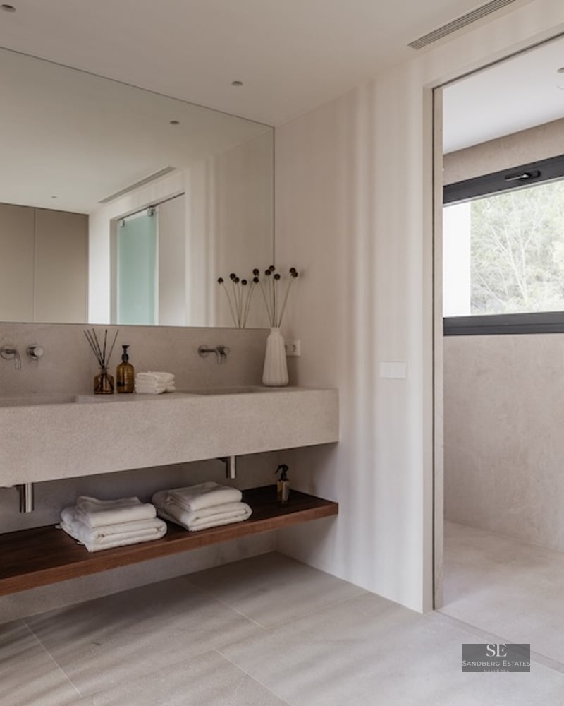 Modern master bathroom featuring a beige stone double vanity, wooden slat wall, and frosted glass sliding door.