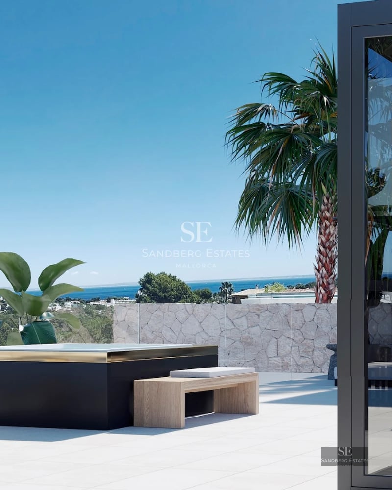 Spacious balcony with sea view. Modern furniture, glass railing, and light-colored tiling. Visible vegetation.