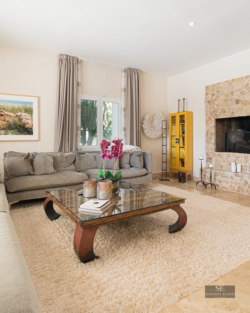 Spacious living room featuring a large grey sectional, a natural stone fireplace, and a glass coffee table on a plush rug.