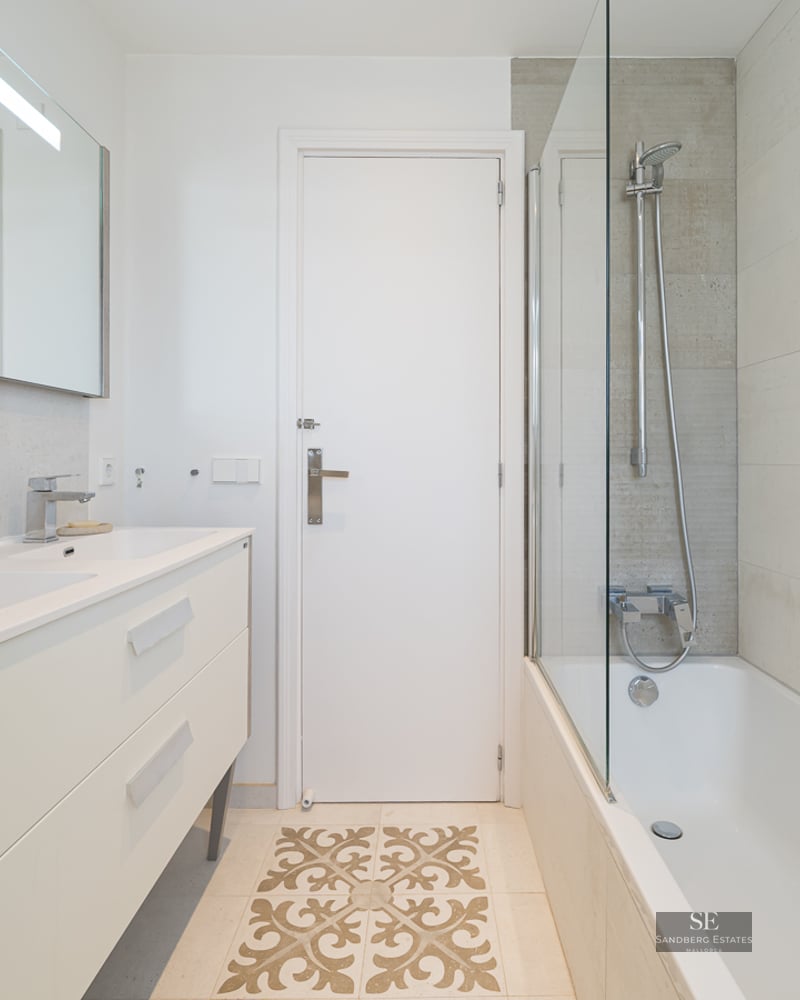 Modern bathroom featuring a cream double vanity, bathtub with glass screen, and decorative floor tile detail.