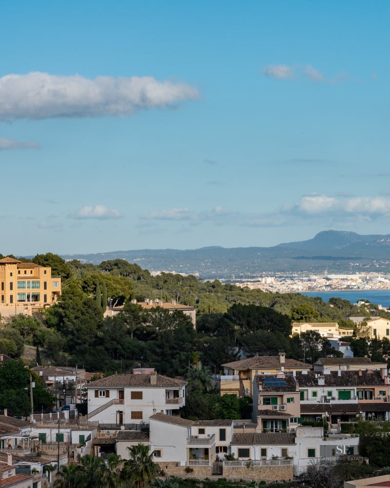 Panoramic landscape view showing a yellow villa, a historical stone castle on a hill, and the Mediterranean Sea in the distance.