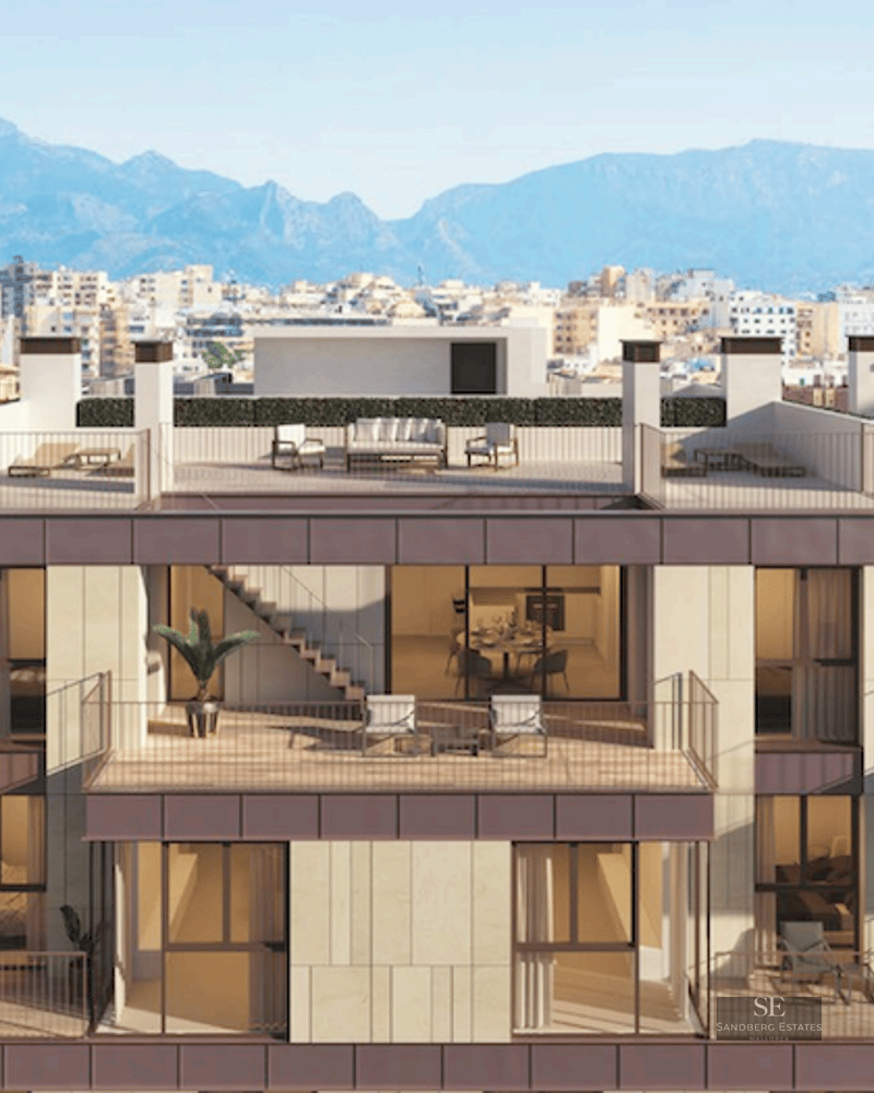 Modern building facade featuring multiple balconies, rooftop terraces, and a backdrop of city and mountains.