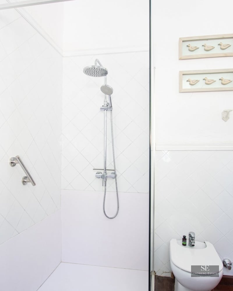 Bright white bathroom featuring a walk-in shower with glass partition, a bidet, and arched built-in shelving with plants.