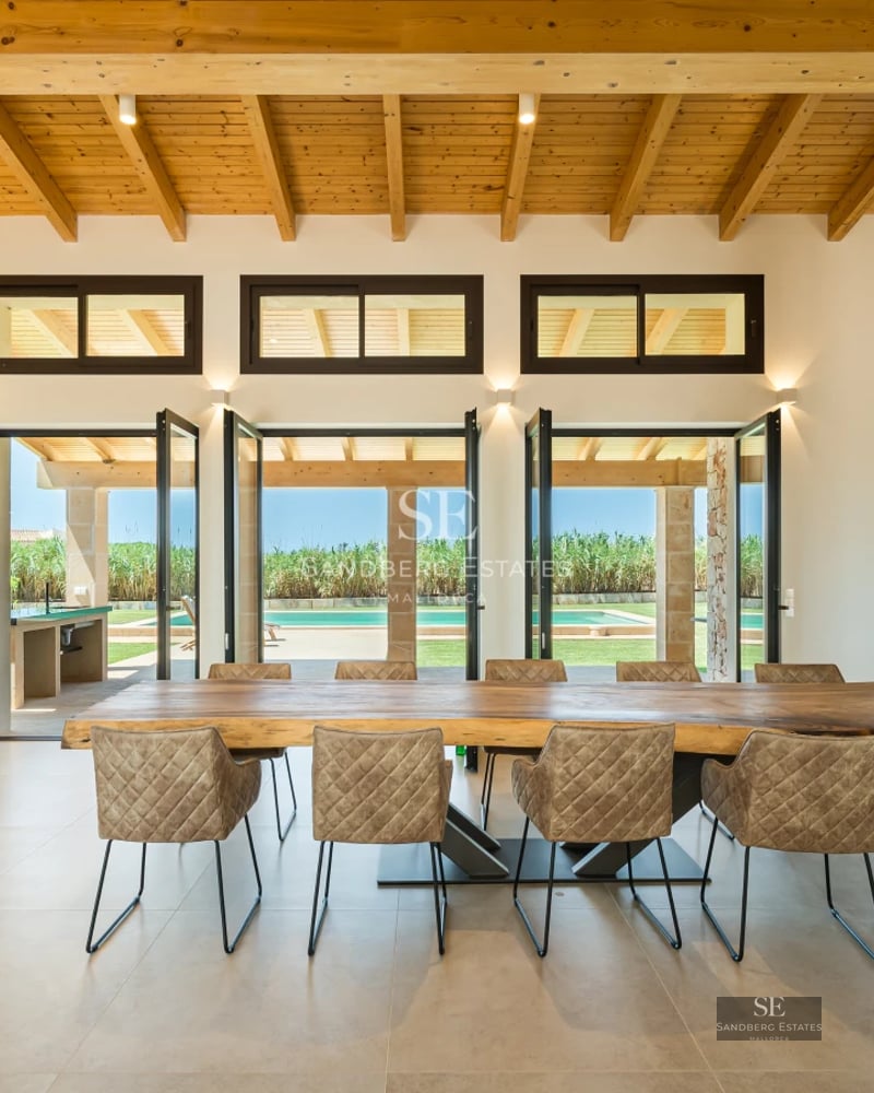 Bright living room with grey sofas, wooden coffee table, and large windows offering exterior views. Minimalist and elegant design.