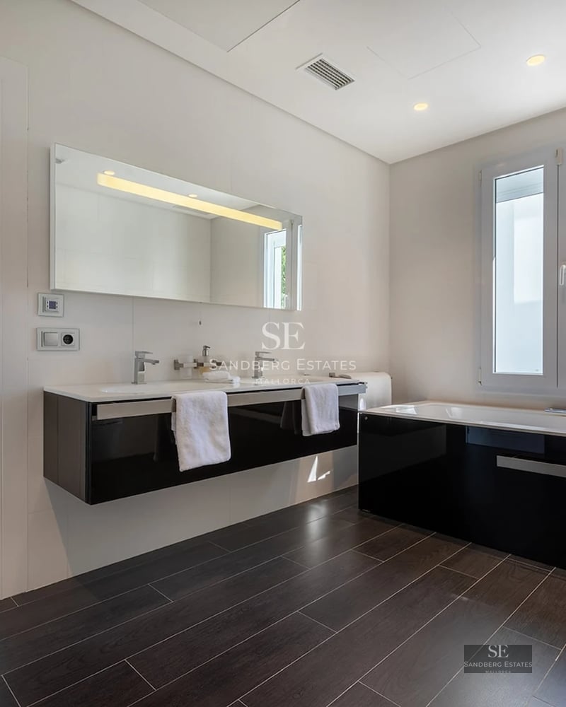 Spacious modern bathroom featuring a black and white double vanity, large mirror, and a bathtub with dark floor tiles.