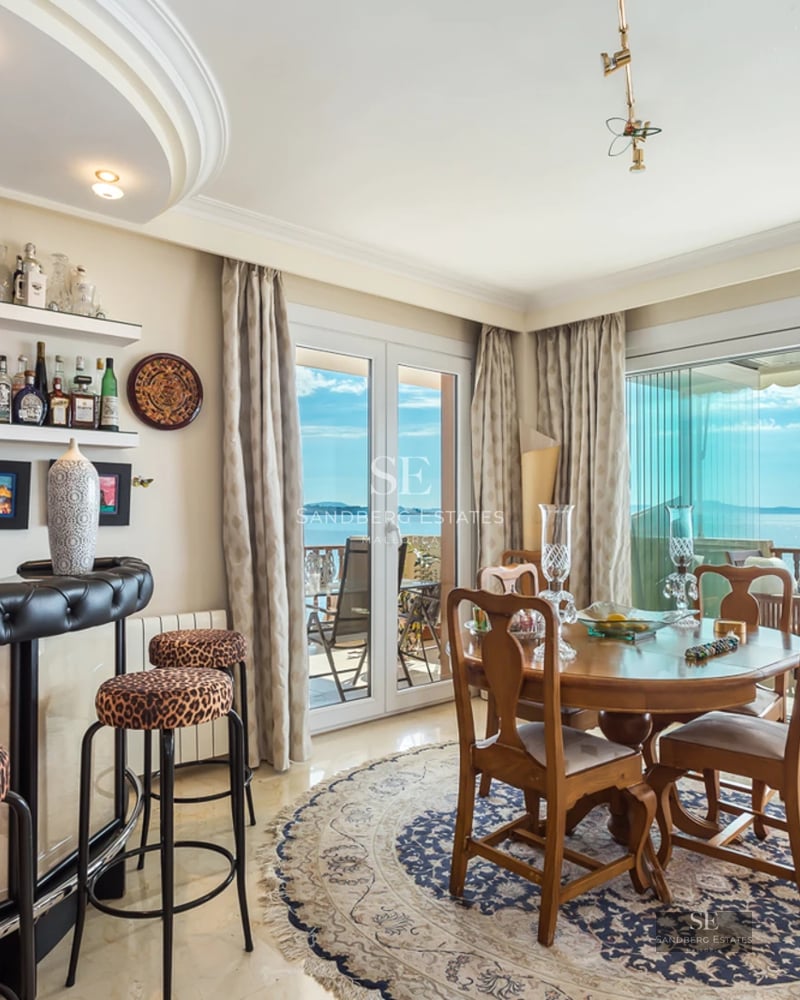Dining area with a wooden table, leopard print stools, a home bar, and glass doors leading to a balcony with sea views.