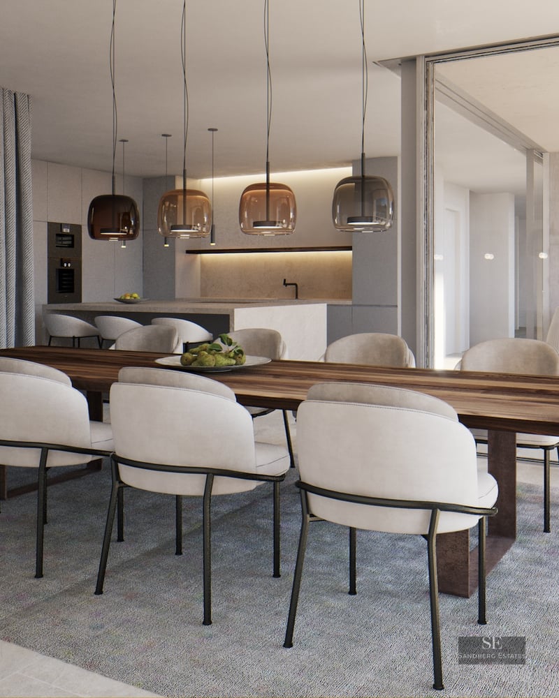 Large wooden dining table with cream chairs and glass pendant lights next to an open terrace and modern kitchen.