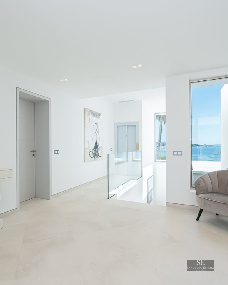 Bright modern hallway with stone floors, glass railings, an elevator, and a large window overlooking the blue sea.