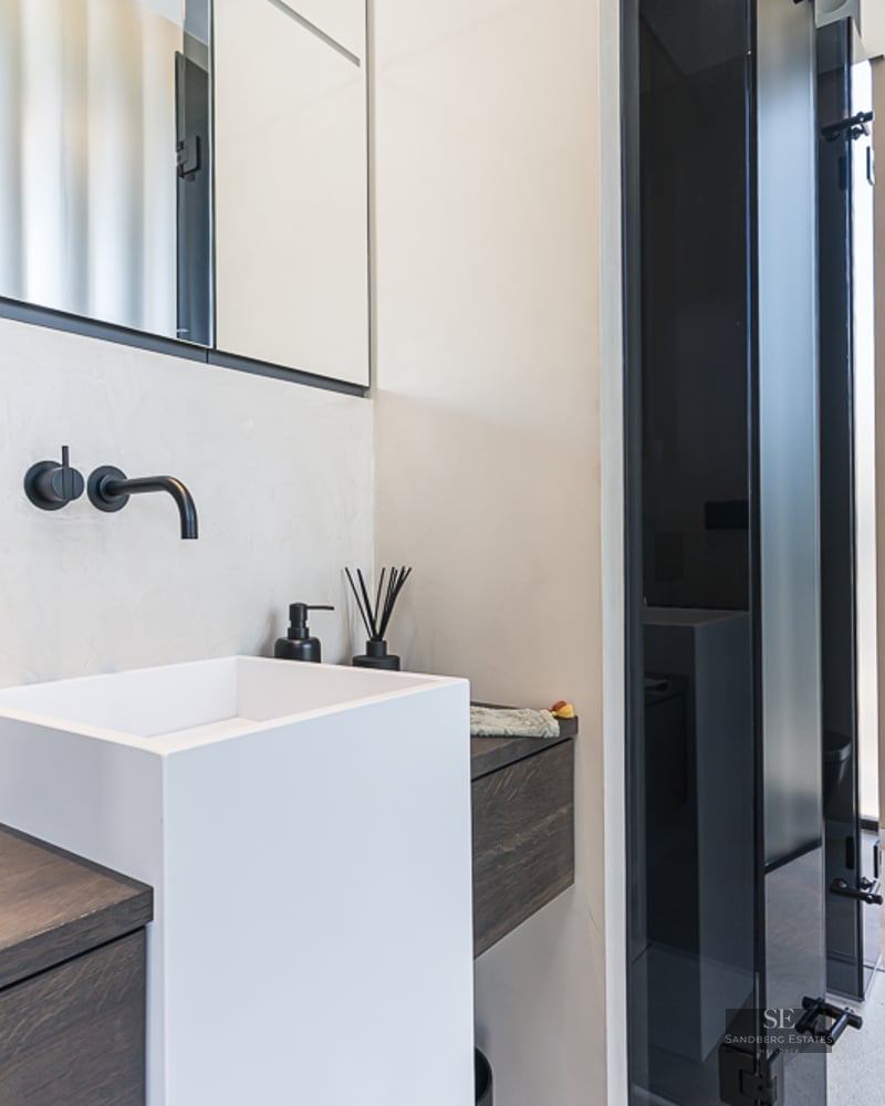White square vessel sink with matte black wall-mounted faucet on dark wood vanity in a modern bathroom.