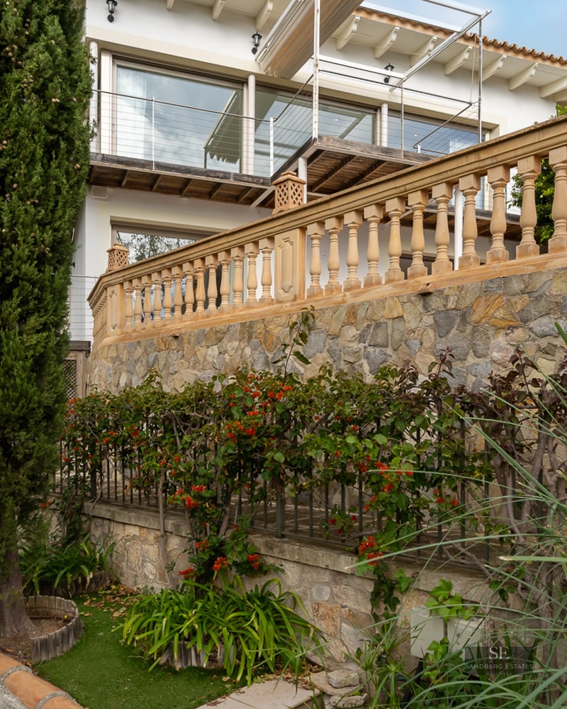 Tiered garden with stone retaining walls, classic balustrades, and lush cypress trees leading to a white villa.