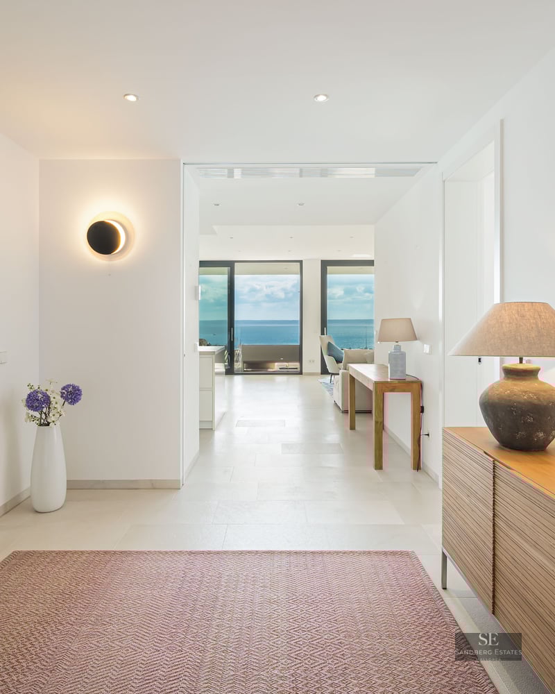 Bright minimalist hallway with wooden furniture and a large mirror, leading to a living room with panoramic ocean views.