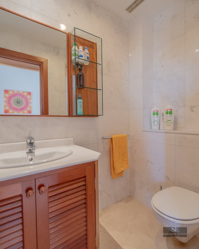 Bathroom featuring marble walls, a wooden vanity unit, a large mirror, and a white toilet.