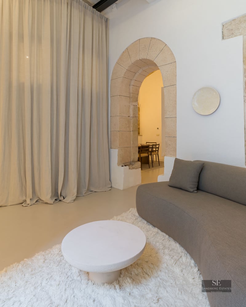 Modern curved sofa on a white shag rug in a room with historic stone arches and soft beige curtains.