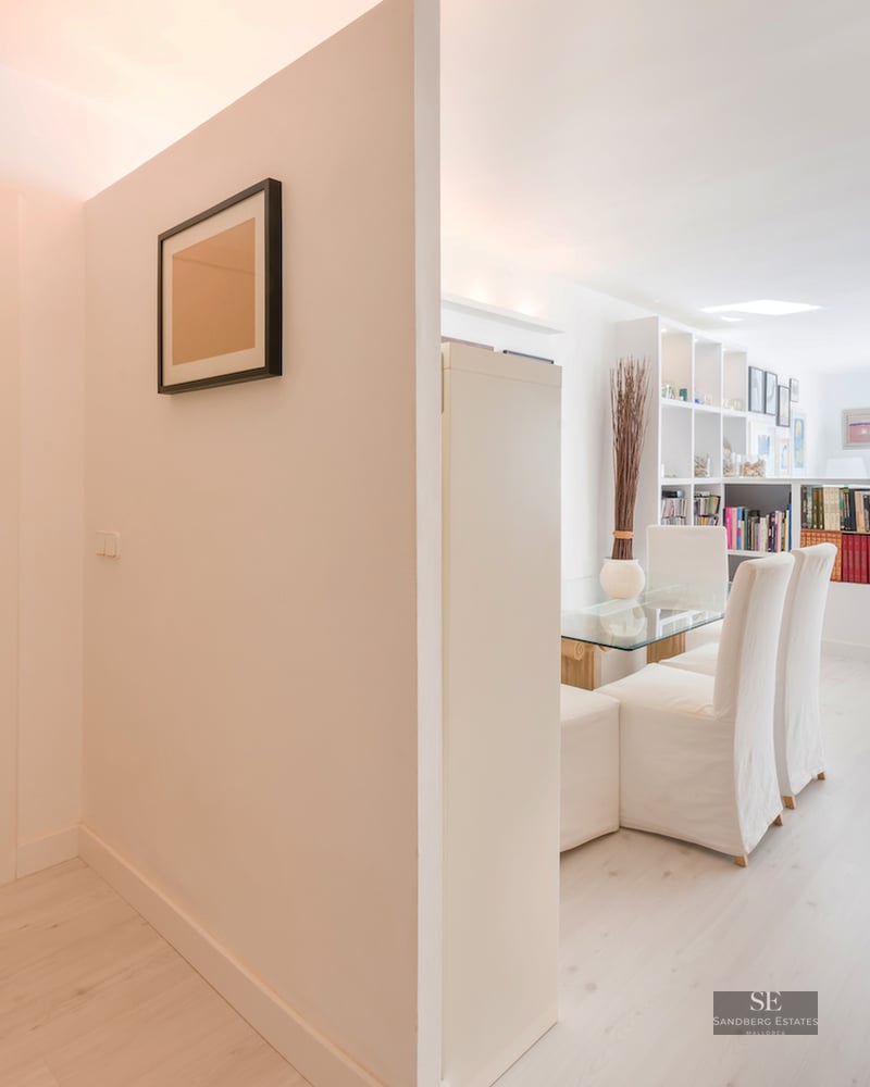 A bright white entryway leading to a minimalist living space with light wood floors and large windows.