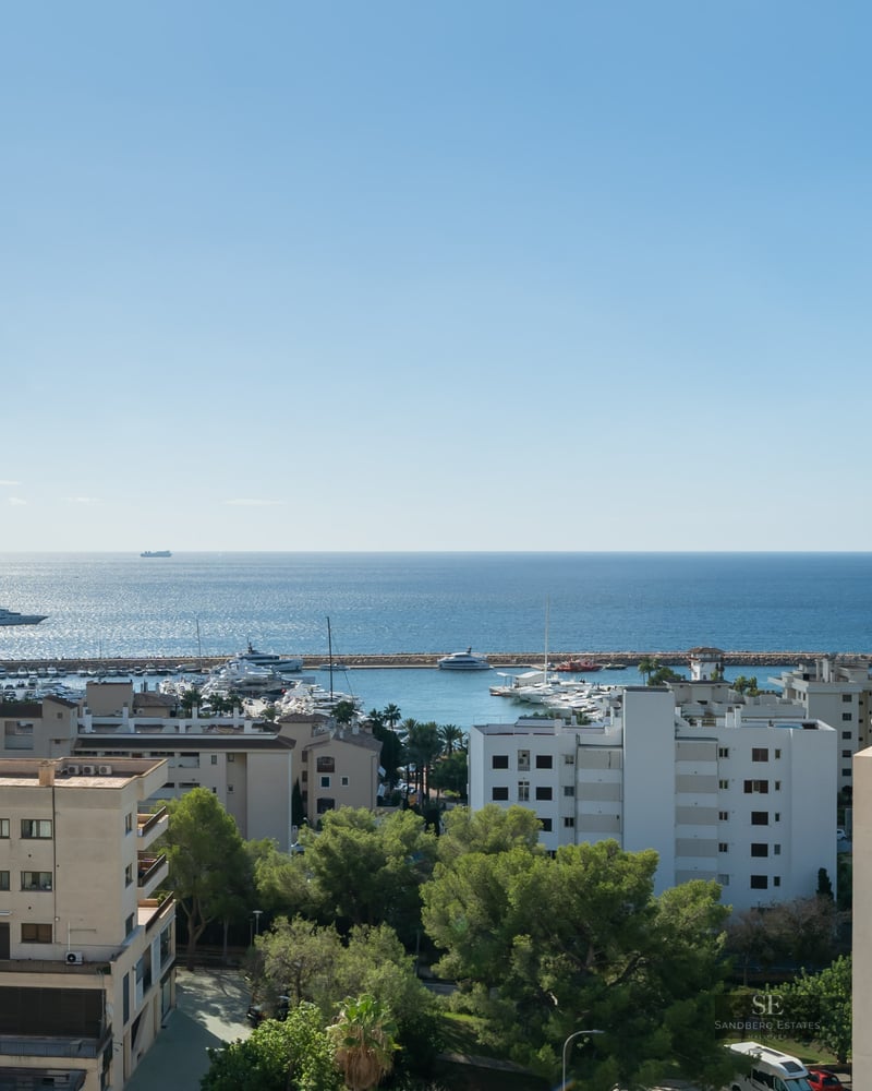 High-angle view of a coastal city, a yacht-filled marina, and the vast blue Mediterranean Sea under a bright sky.