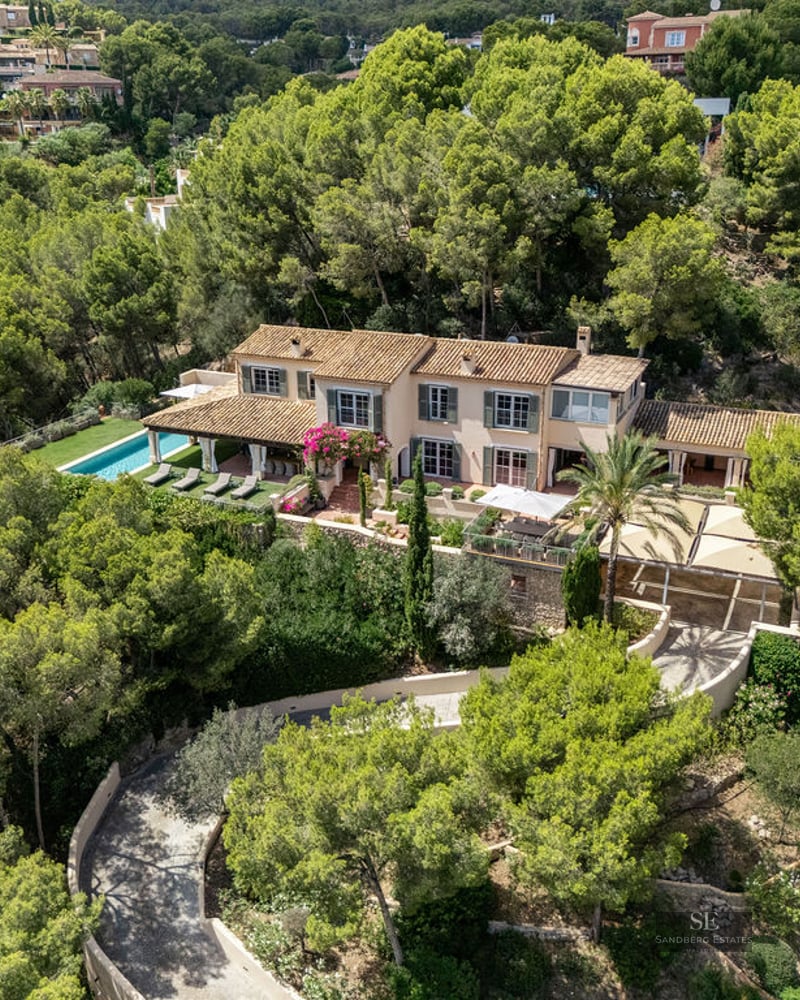 Aerial shot of a luxury Mediterranean villa with a pool, terracotta roof, and lush green forest surroundings.
