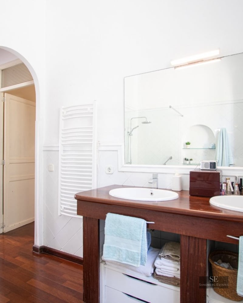 Bathroom featuring a wooden double vanity with two white sinks, a large mirror, and dark wood floors.