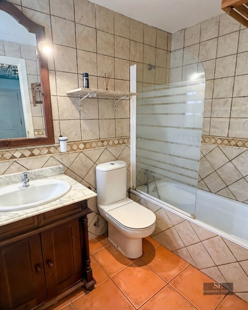 Bathroom featuring a bathtub, toilet, marble-top vanity, and earth-toned ceramic tiling.
