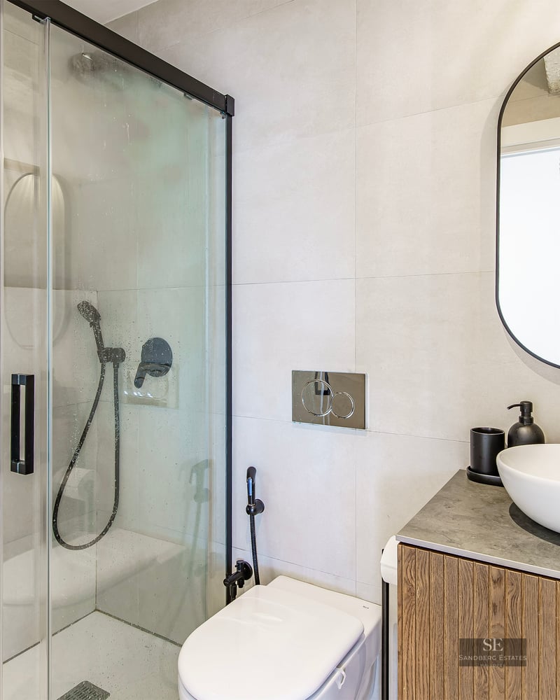 Contemporary bathroom featuring a glass walk-in shower with black hardware, a wooden vanity, and an oval mirror.