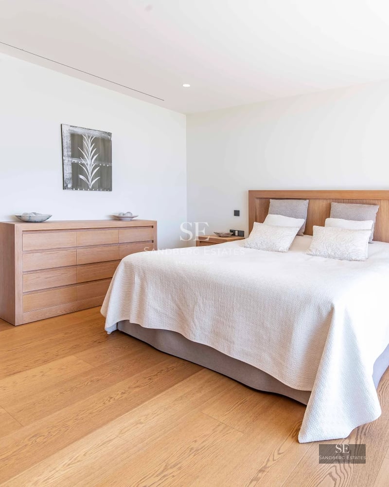 Spacious living room with picture windows, light wood floors, minimalist decor, and panoramic sea views. Beige sofa and modern rug.