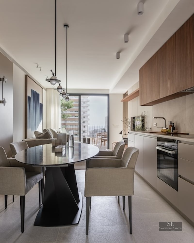 Contemporary dining room with oval black table, grey chairs, and a minimalist integrated kitchen with balcony access.