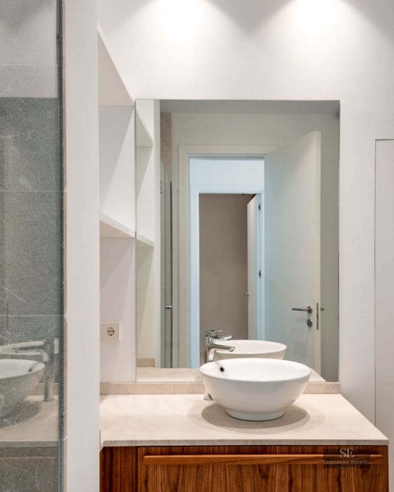White ceramic vessel sink on a wood vanity, large mirror, and grey veined stone shower wall.