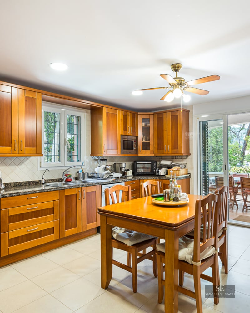Traditional wooden kitchen with granite counters, dining table, and glass doors leading to a terrace.