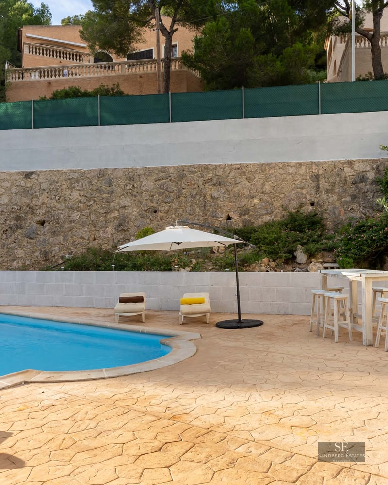 Piscine privée avec chaises longues, parasol blanc et mur en pierre rustique en arrière-plan.