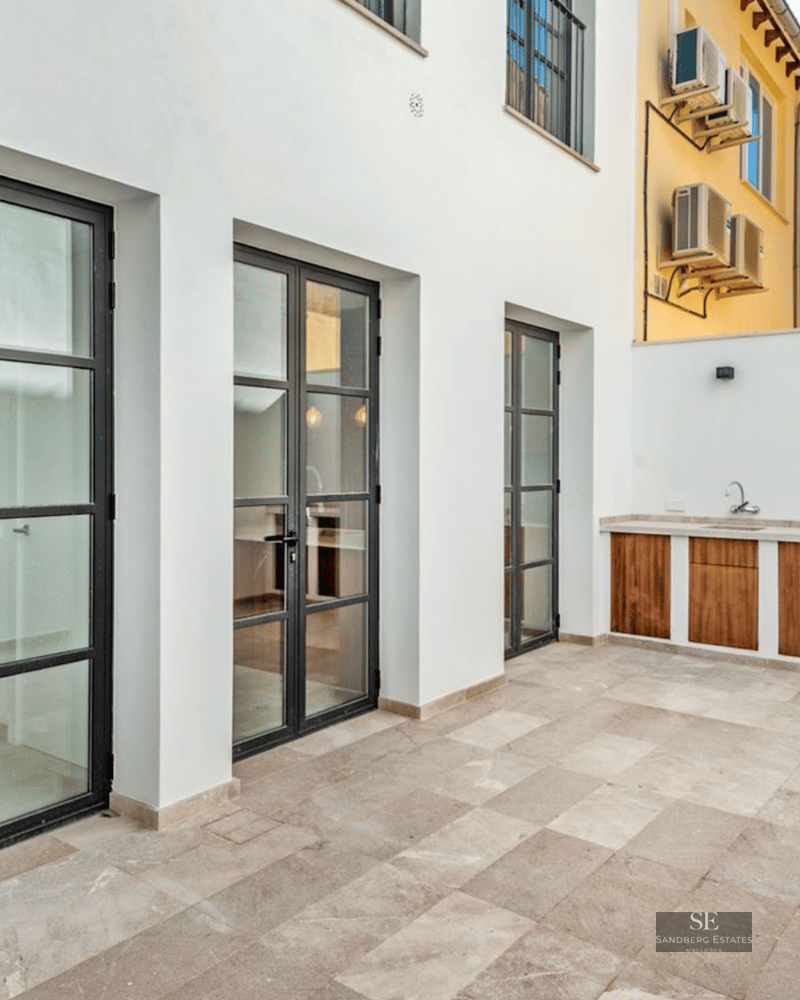 Modern terrace featuring stone tiling, black industrial glass doors, and a wood-accented outdoor kitchen unit.