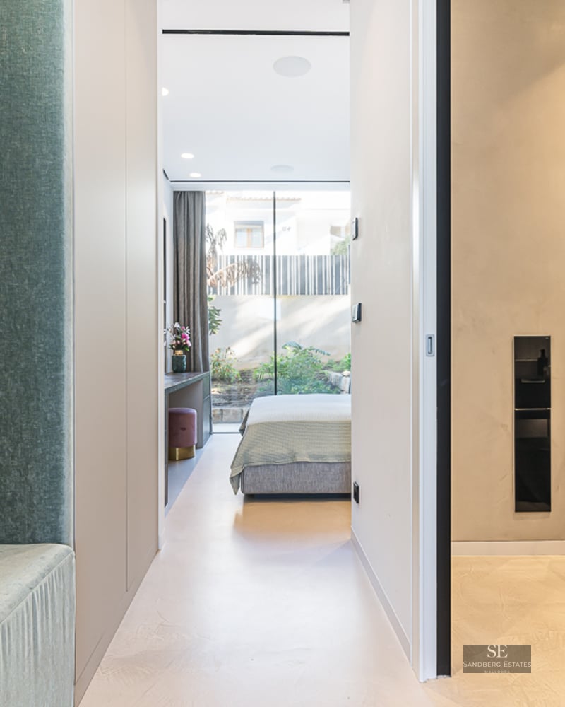 Minimalist hallway leading to a bright bedroom with floor-to-ceiling windows and outdoor garden views.