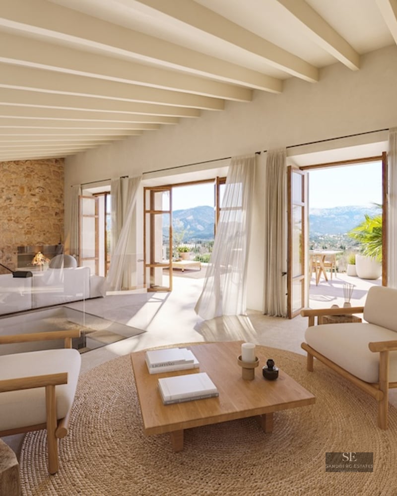 Airy living room with stone walls, beamed ceilings, and glass doors opening to a scenic mountain terrace.
