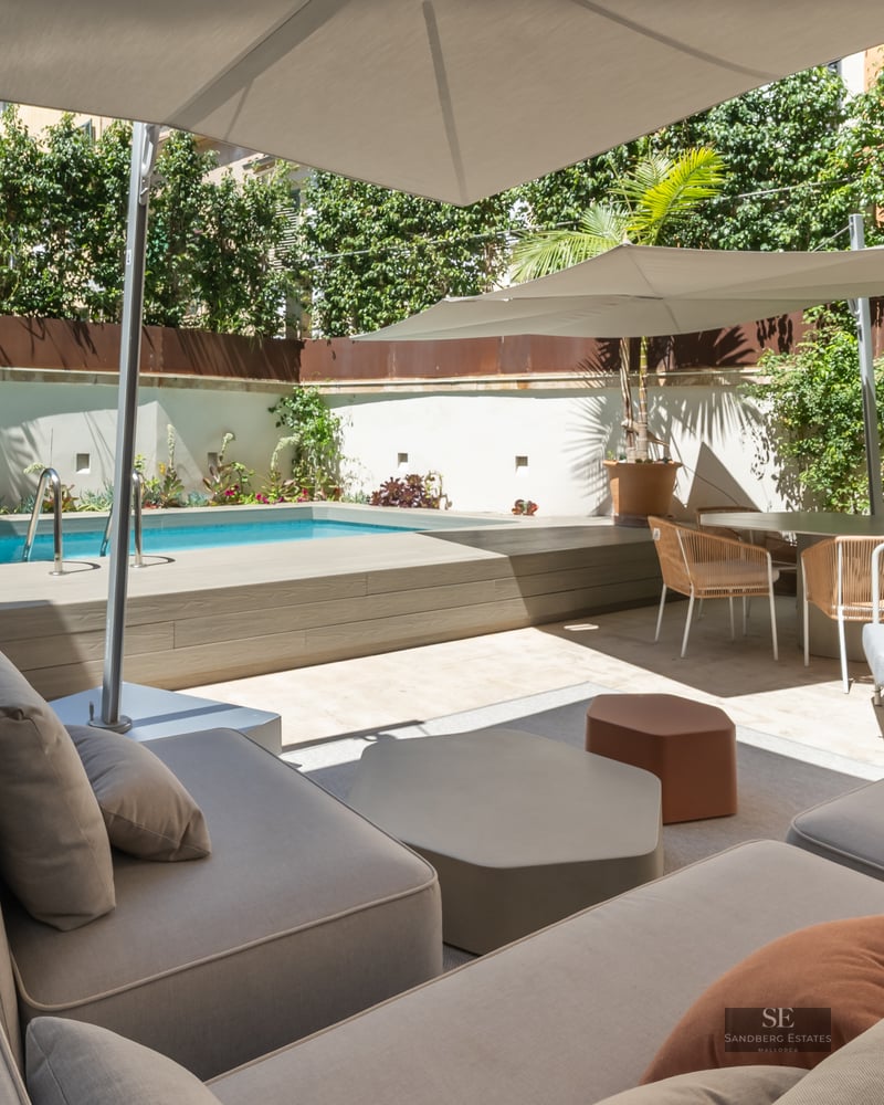 Sun-drenched terrace featuring a private pool, modern grey sofas with terracotta pillows, and large white umbrellas.