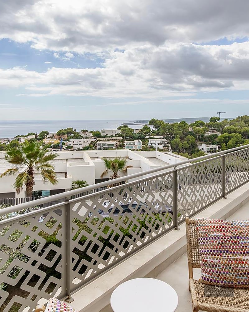 Modern balcony with decorative patterned railing, wicker chair, and views of the Mediterranean coast under a cloudy sky.