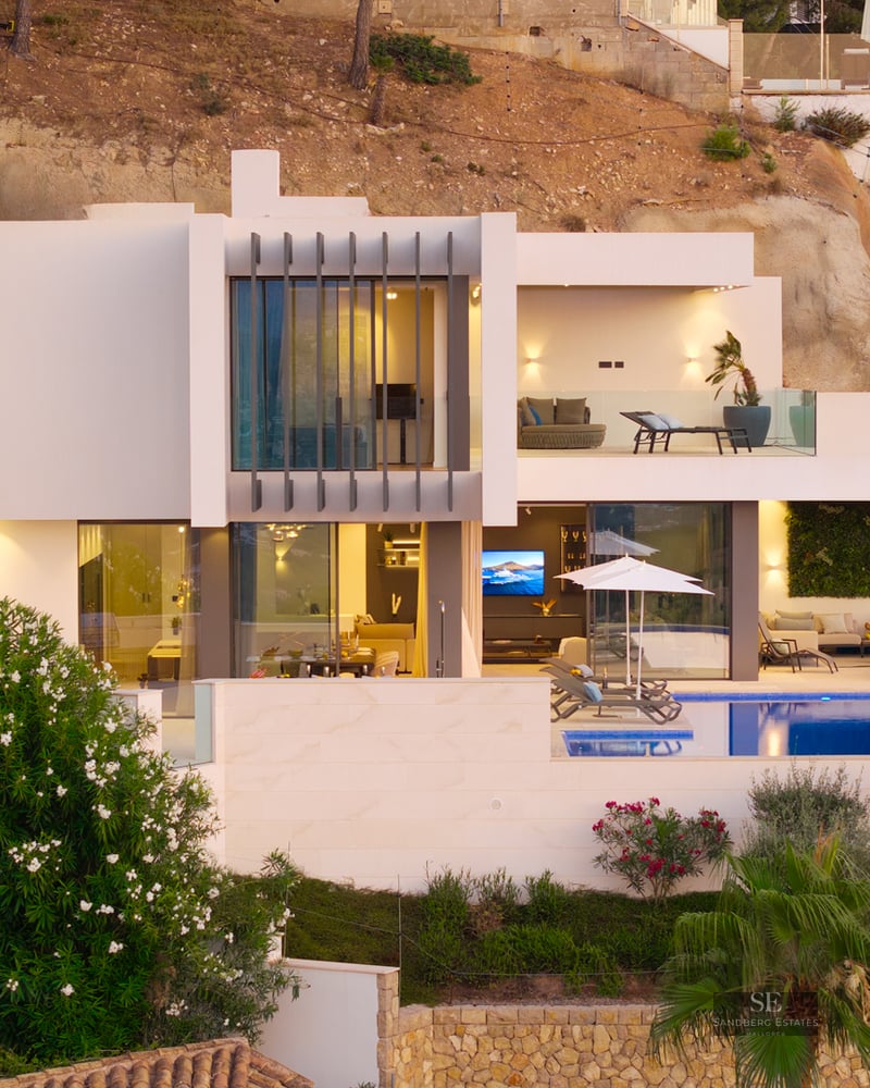 Modern white multi-level villa with a swimming pool, terraces, and large glass windows built into a rocky hillside.