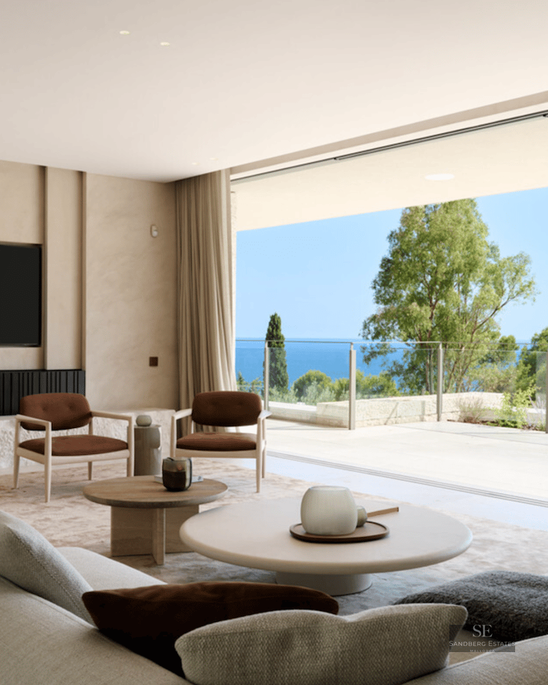 Minimalist living room with beige sofa and armchairs opening onto a terrace with a stunning Mediterranean sea view.